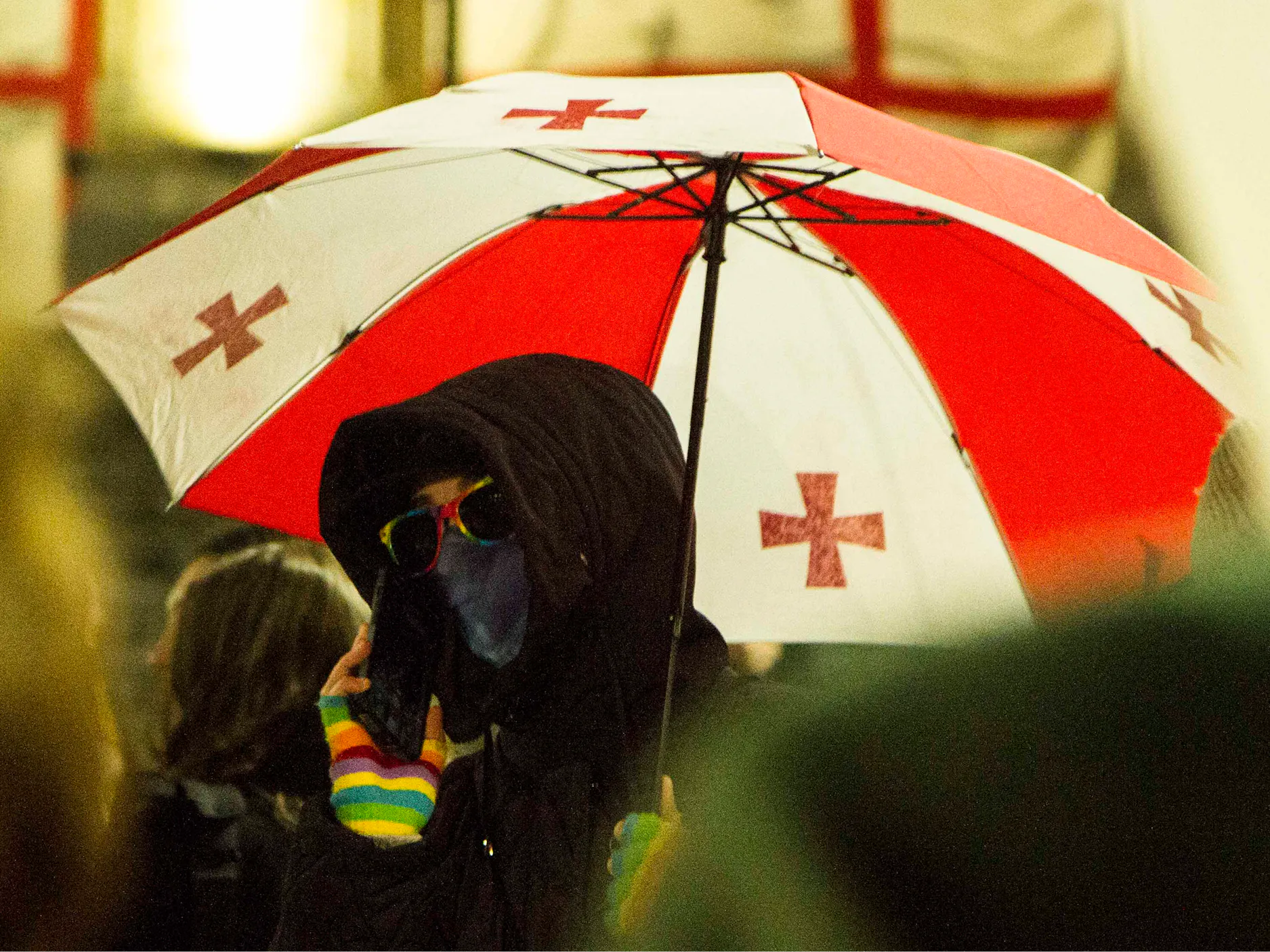 Protestnik z zakritim obrazom in dežnikom z motivom gruzijske zastave